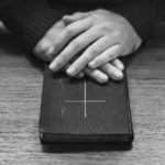 Hands over bible on wooden table