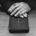 Hands over bible on wooden table
